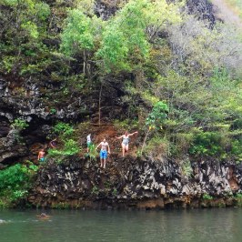 a group of people standing next to a body of water surrounded by trees