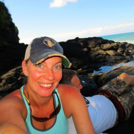 a woman sitting on a rock next to a body of water