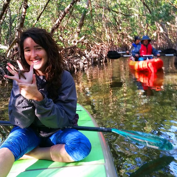 a woman riding on the back of a boat next to a tree