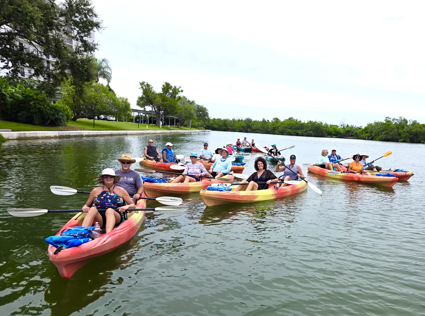 Group of people kayaking on a calm river near a tree-lined shore.
